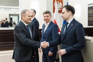 Premier Donald Tusk ściskający ręce z ministrem finansów i gospodarki Andrzejem Domańskim. W tle przygląda się temu minister Jan Grabiec.
