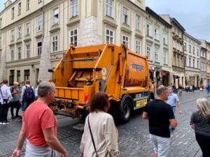 Pomarańczowa śmieciarka jadąca ulicą Szewską w Krakowie.