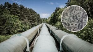 W centrum zdjęcia trzy nitki rurociągu idące przez las iglasty w okresie letnim. W prawym, górnym rogu w kółku znajduje się stos banknotów studolarowych.