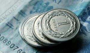 Na zdjęciu stosik monet jednozłotowych ułożony w wieżę stojącą na banknocie 50-złotowym.