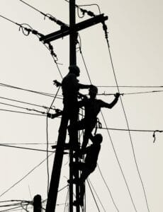 Trzech mężczyzn stoi na słupie wysokiego napięcia i dokonuje napraw