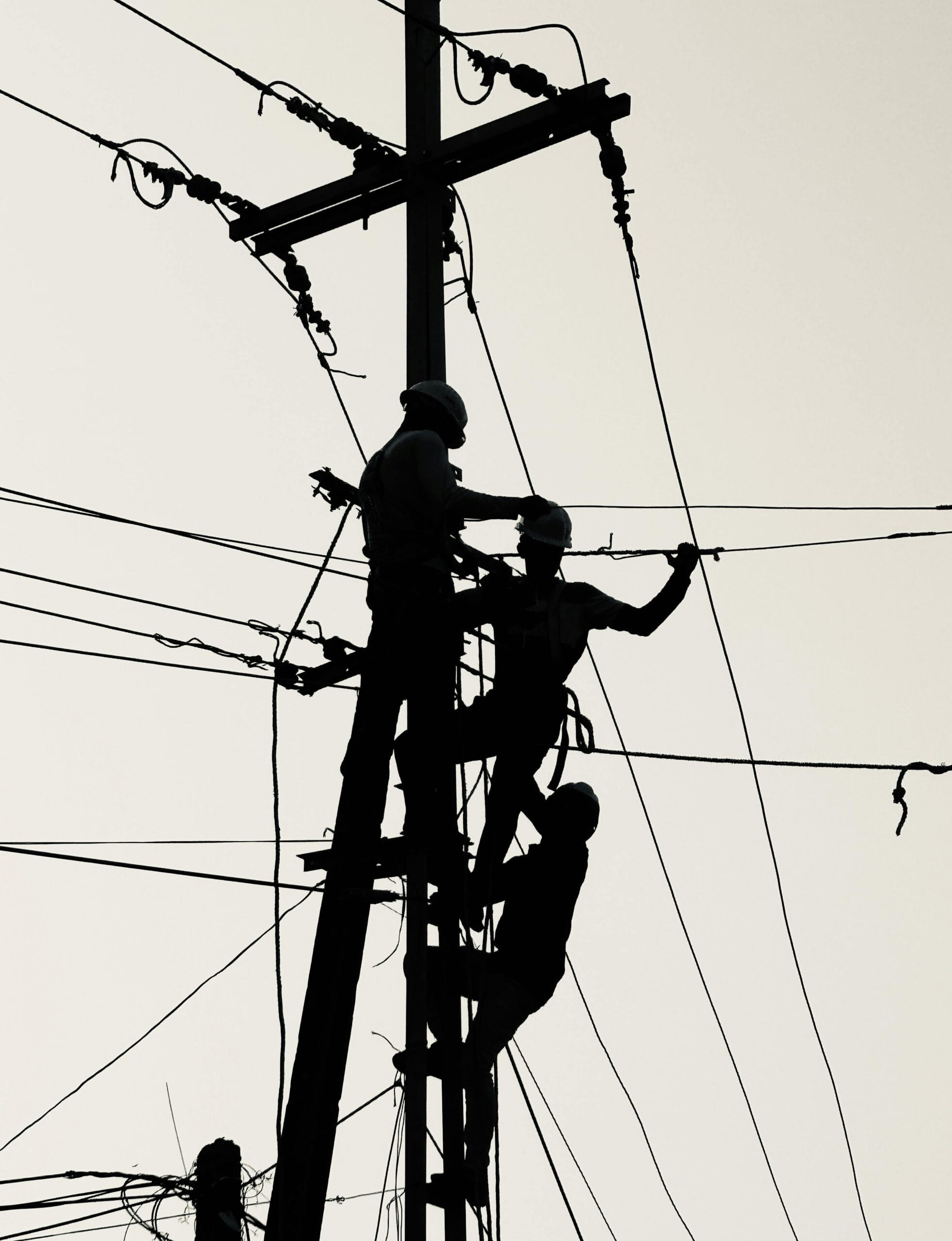 Trzech mężczyzn stoi na słupie wysokiego napięcia i dokonuje napraw