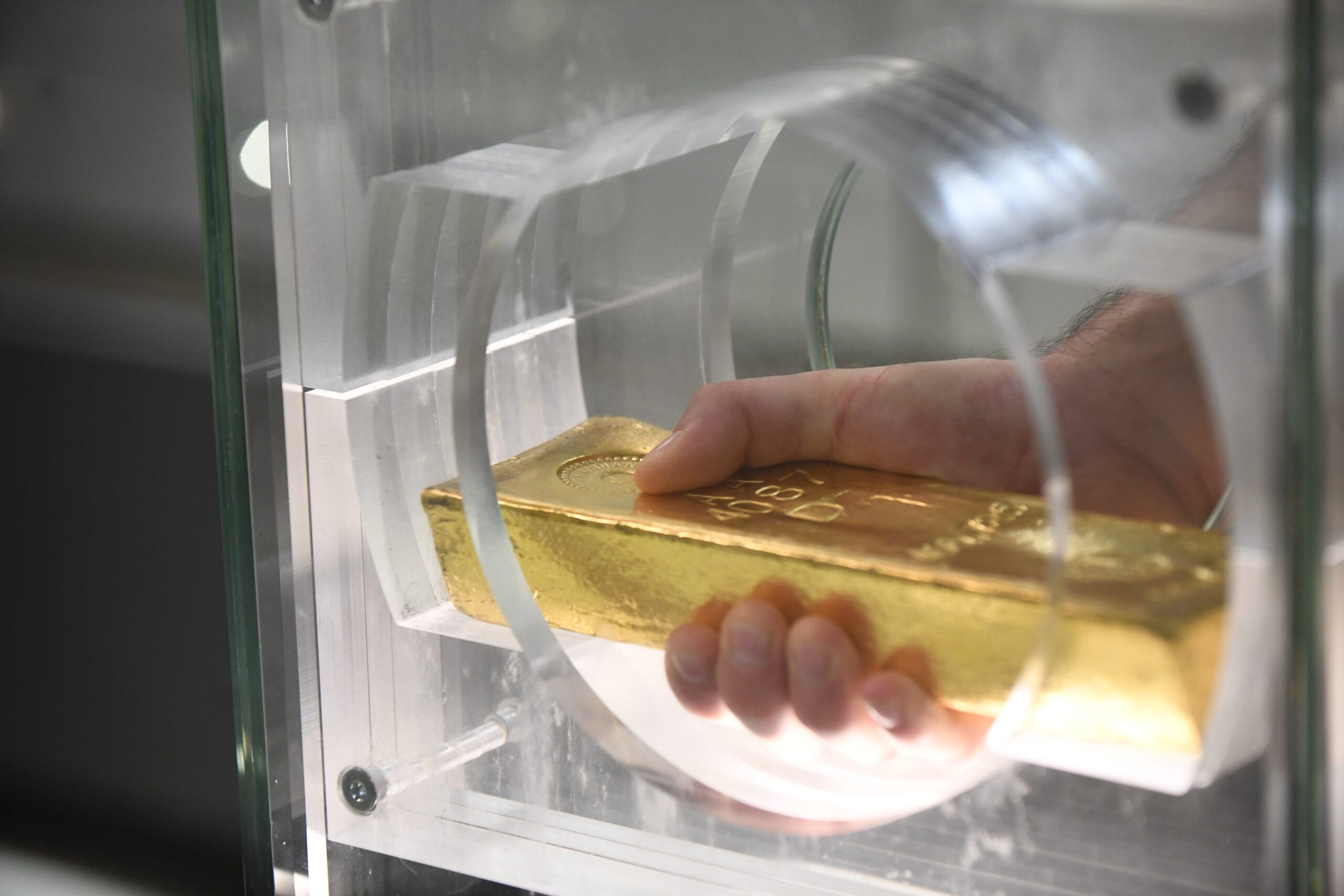 Złota sztaba w ręce mężczyzny widoczna zza szklanego zabezpieczenia.