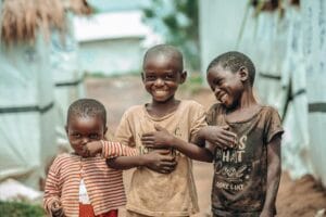 Trzech czarnoskórych chłopaków śmieje się wprost do kamery na tle afrykańskiej wioski