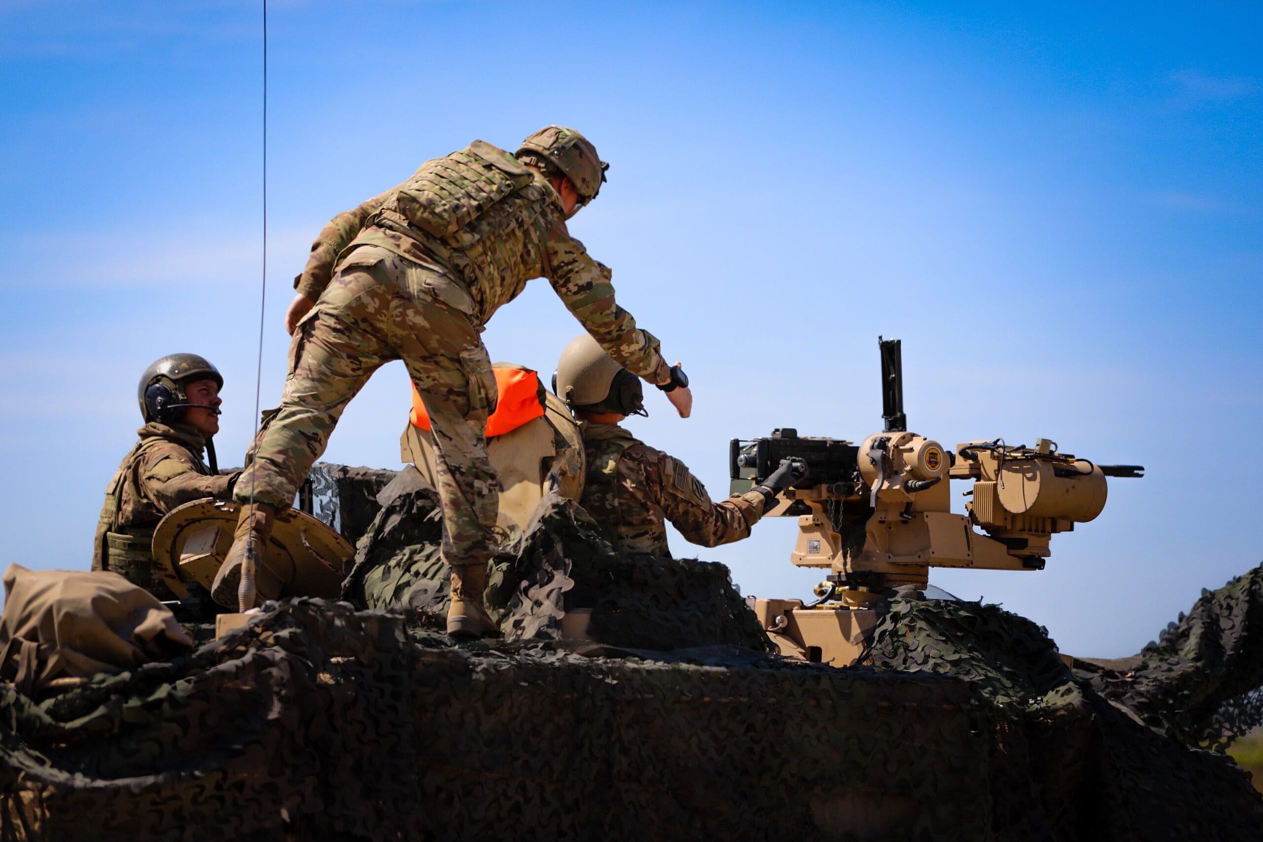 Żołnierze w mundurach i kamizelkach pracujący na czołgu typu Abrams.