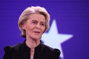 Ursula von der Leyen ze skupioną miną na tle białej gwiazdy na niebieskim tle.