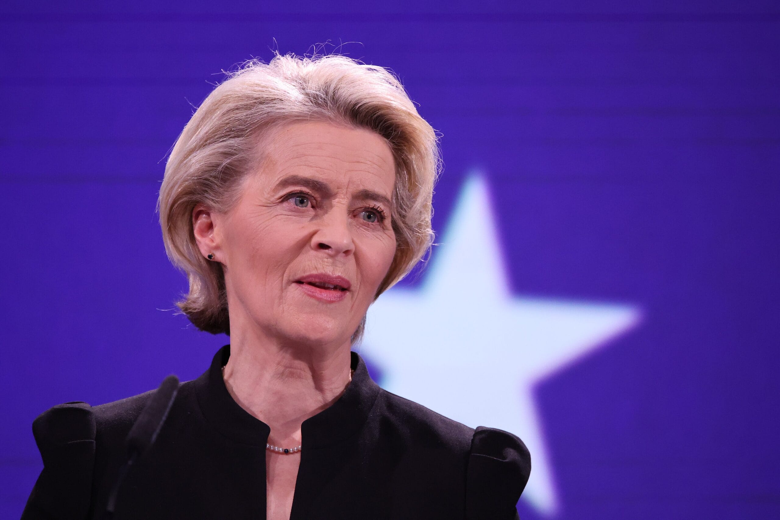 Ursula von der Leyen ze skupioną miną na tle białej gwiazdy na niebieskim tle.