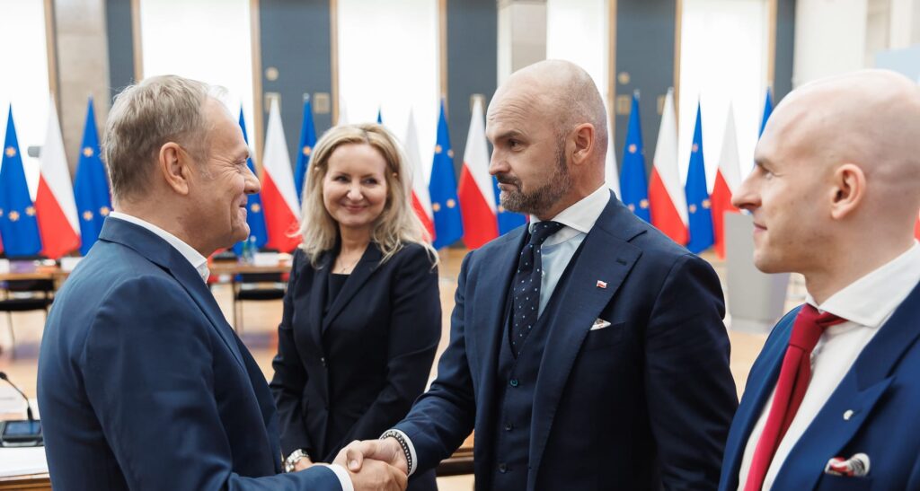 Premier Donald Tusk ściskający rękę Rafała Brzoski. Przyglądają się temu Magdalena Burnat i Ryszard Chmura