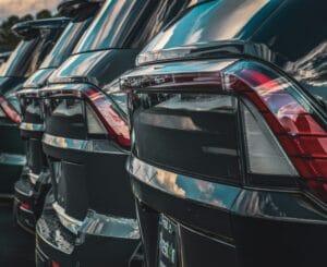 Zdjęcie przedstawia tyły ustawionych w rzędzie czarnych samochodów