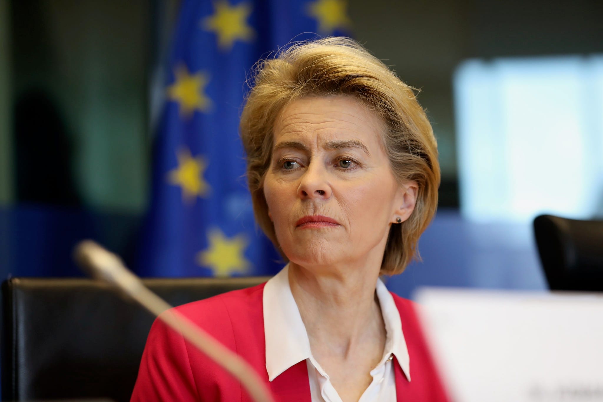 Ursula von der Leyen w czerwonej marynarce podczas posiedzenia na tle flagi unijnej