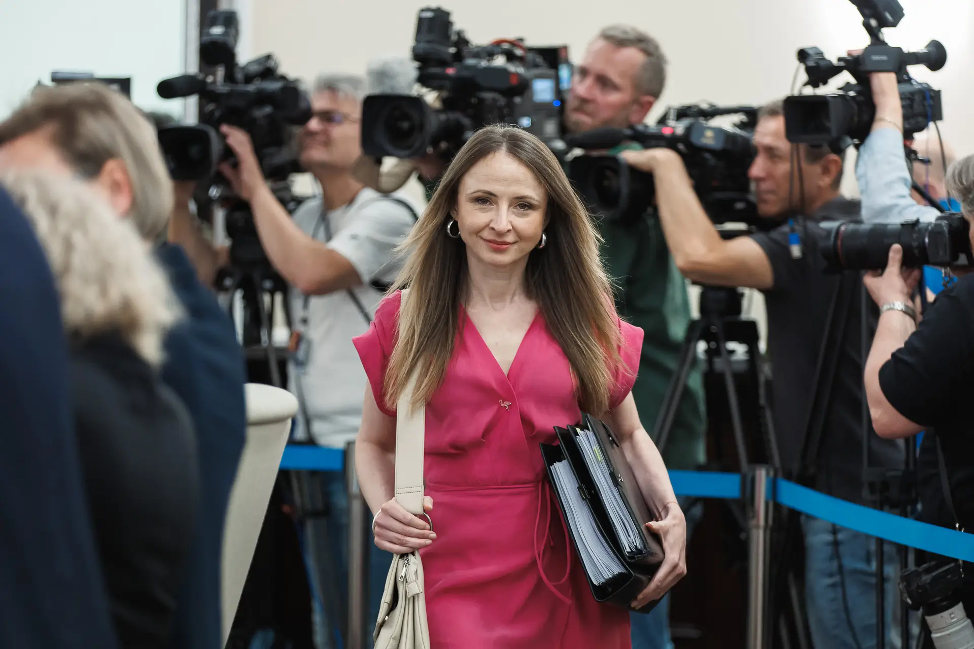 Agnieszka Dziemianowicz-Bąk w różowej sukience wchodzi na posiedzenie rządu drogą wytyczoną między operatorami kamer.