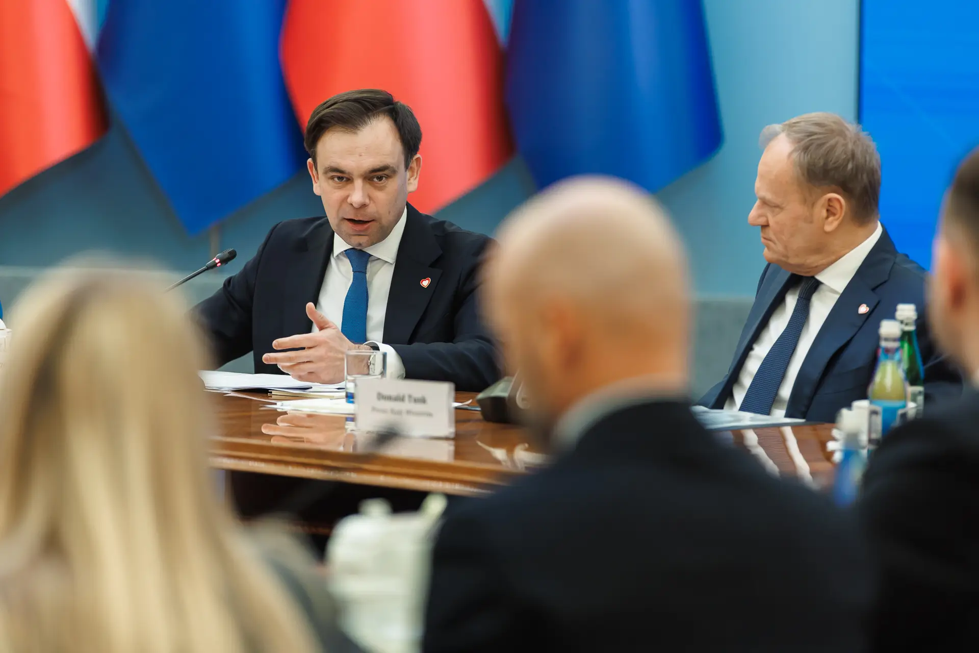 Andrzej Domański przemawia podczas spotkania z przedsiębiorcami. Po jego prawej siedzi wpatrzony w niego Donald Tusk.