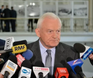 Leszek Miller w 2015 r. w Sejmie przed mikrofonami mediów, patrzący w bok.