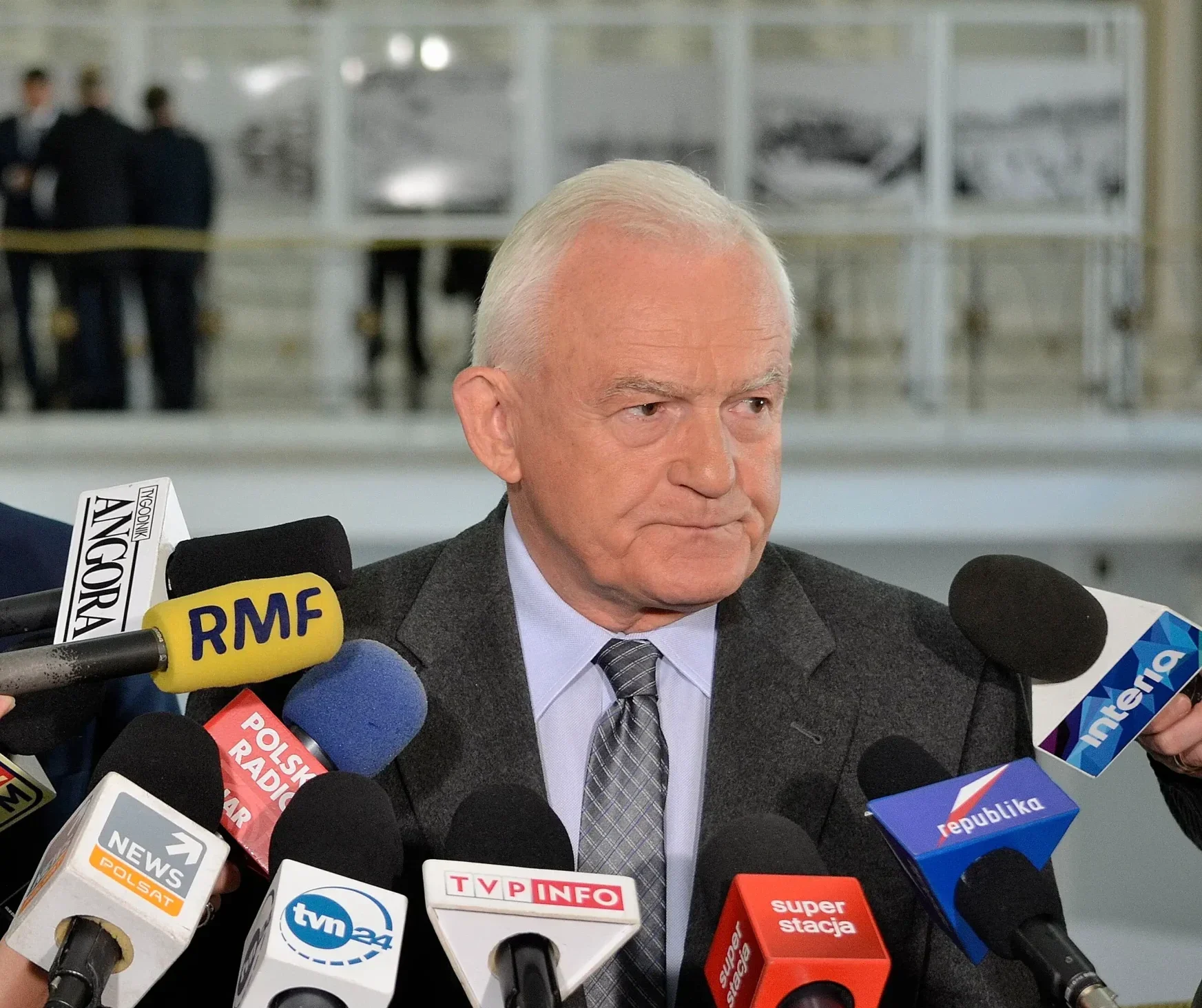 Leszek Miller w 2015 r. w Sejmie przed mikrofonami mediów, patrzący w bok.