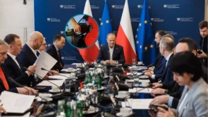 Posiedzenie rządu; elegancko ubrani politycy siedzą przy długim stole, na którego końcu zasiada Donald Tusk. Za premierem znajdują się cztery flagi - po dwie Polski i Unii Europejskiej. Na flagach znajduje się małe kółeczko ze zdjęciem w środku, przedstawiającym rękę tankującą paliwo do baku samochodu.