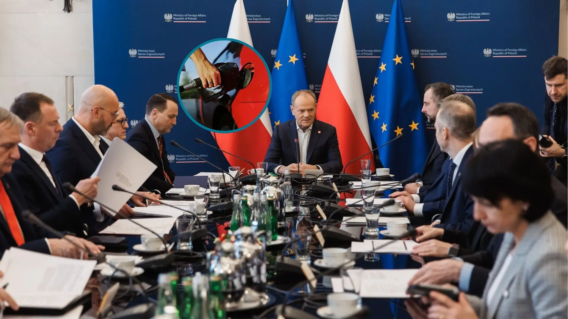 Posiedzenie rządu; elegancko ubrani politycy siedzą przy długim stole, na którego końcu zasiada Donald Tusk. Za premierem znajdują się cztery flagi - po dwie Polski i Unii Europejskiej. Na flagach znajduje się małe kółeczko ze zdjęciem w środku, przedstawiającym rękę tankującą paliwo do baku samochodu.