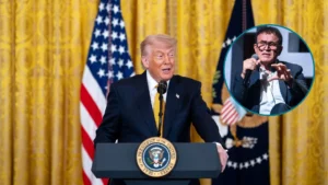 Donald Trump w czasie konferencji prasowej w Białym Domu. Przemawia na tle złotej kotary i dwóch flag USA. W prawym rogu w kółku Nouriel Roubini z mikrofonem w czasie panelu.