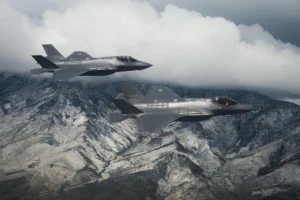 Dwa myśliwce F-35 nad górskim krajobrazem.