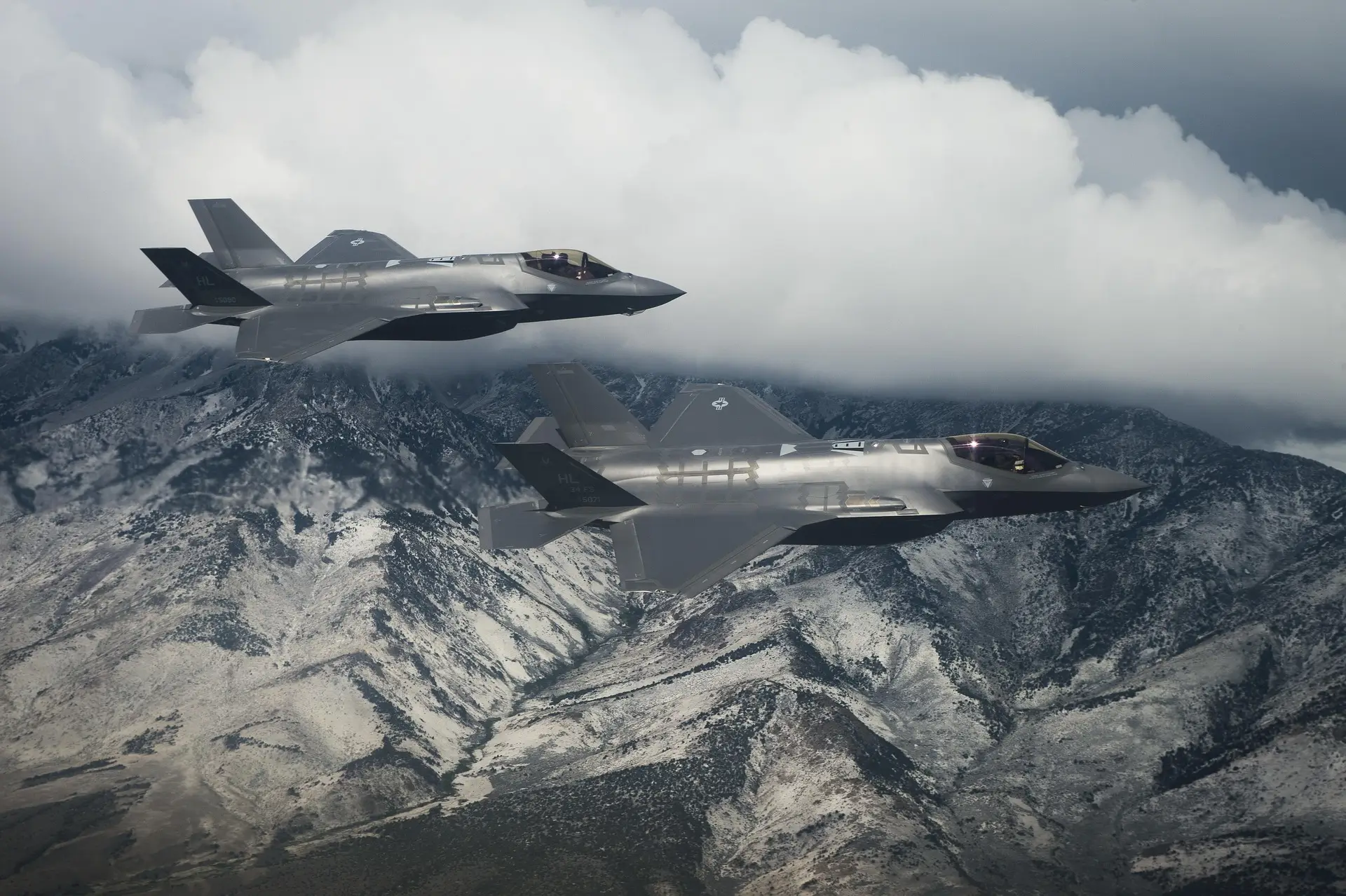 Dwa myśliwce F-35 nad górskim krajobrazem.