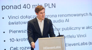 Mati Staniszewski na konferencji prasowej przy mównicy z napisem "ElevenLabs". Za nim slajd, na któym wybija się hasło "ponad 40 mln PLN"