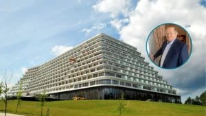 Ogromna bryła hotelu w Pobierowie widziana z ziemi z zielonym otoczeniem. Obok niej Tadeusz Gołębiewski w garniturze w kółku.