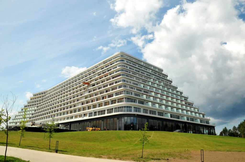 Ogromna bryła hotelu w Pobierowie widziana z ziemi z zielonym otoczeniem.